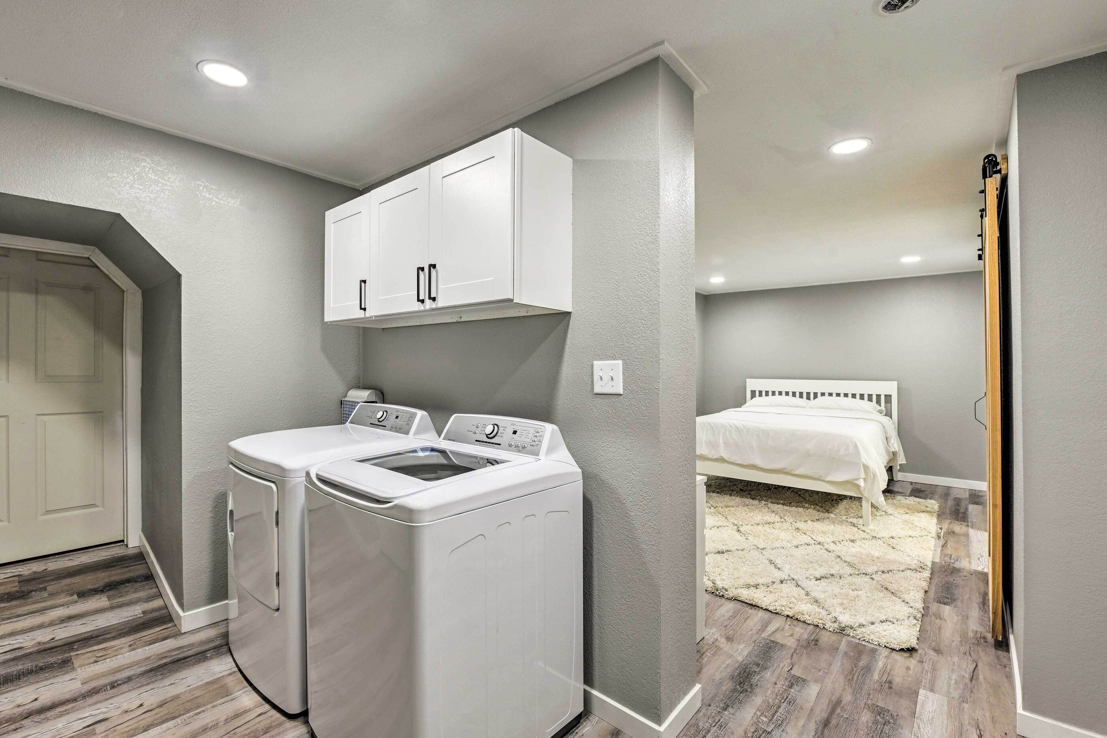 A laundry room with a washer and dryer, a bed with a white headboard, and a gray wall.