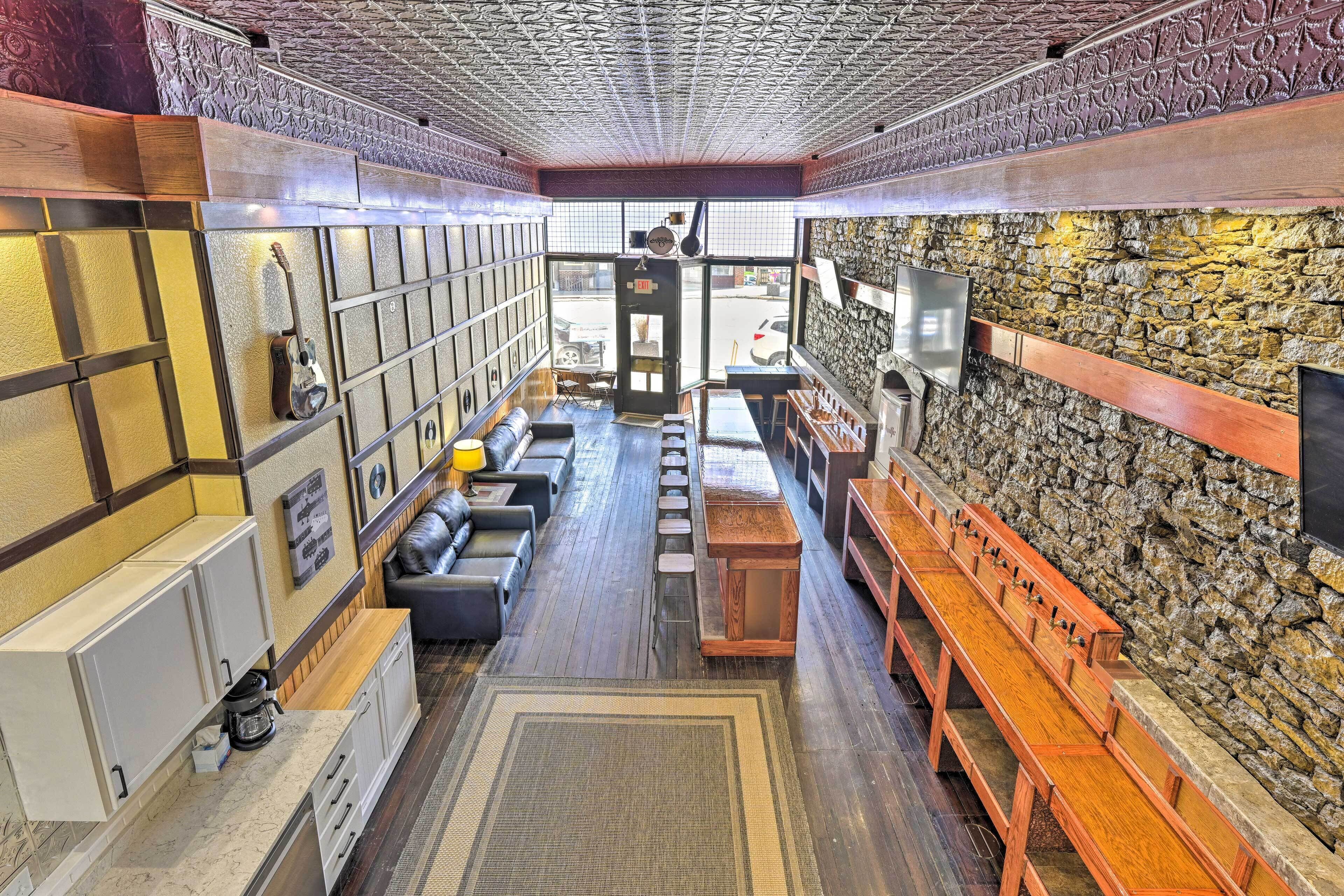 Un interior acogedor con una pared de piedra, bancos de madera y una zona de estar con cojines.
