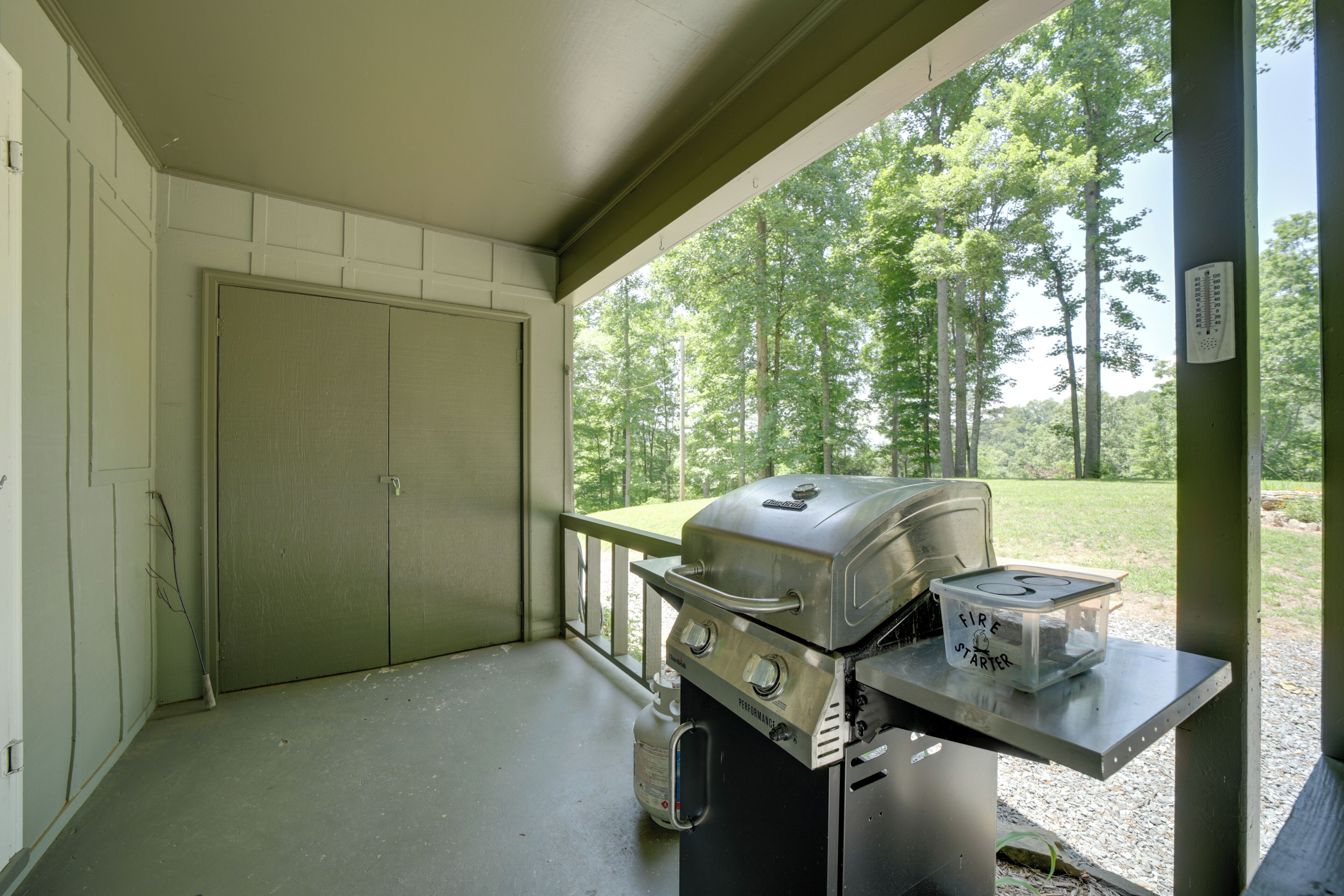 Une véranda couverte avec un barbecue et un allume-feu sur une table.