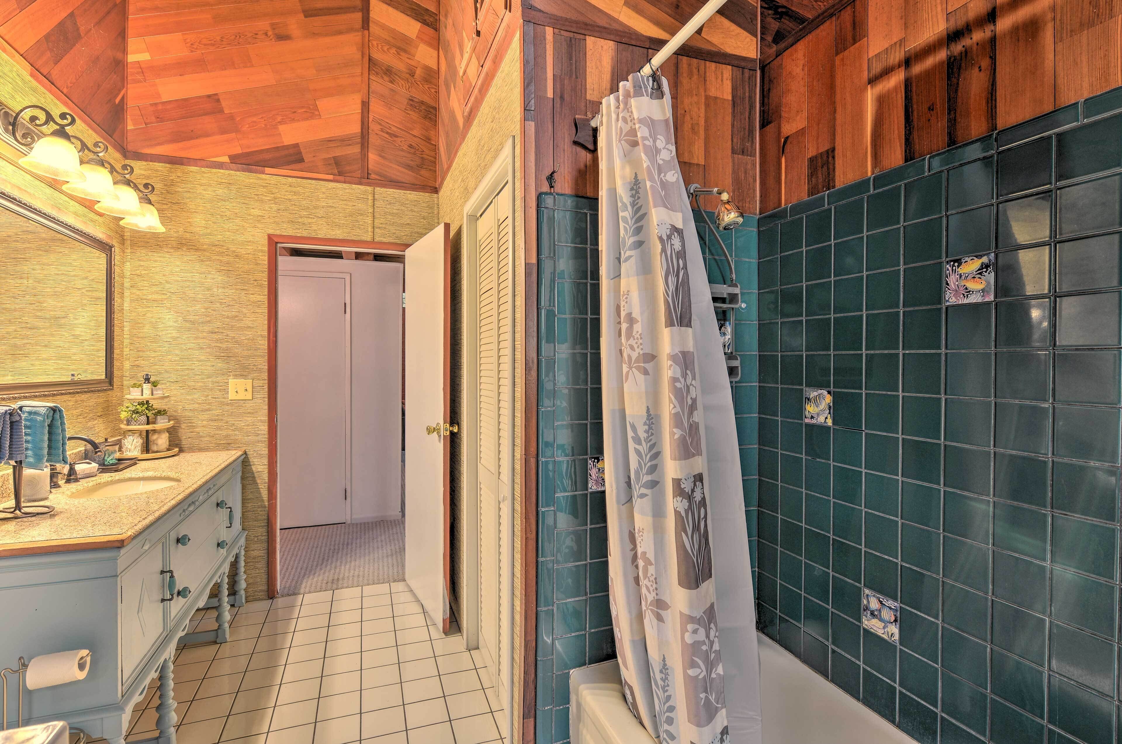 A bathroom with a wooden ceiling, a sink with a mirror, a shower with a curtain, and a tiled wall.