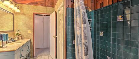 A bathroom with a wooden ceiling, a sink with a mirror, a shower with a curtain, and a tiled wall.