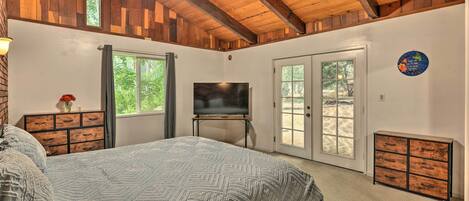Un dormitorio con una cama grande, televisión, cómoda y puerta corrediza de vidrio que da a un espacio exterior.