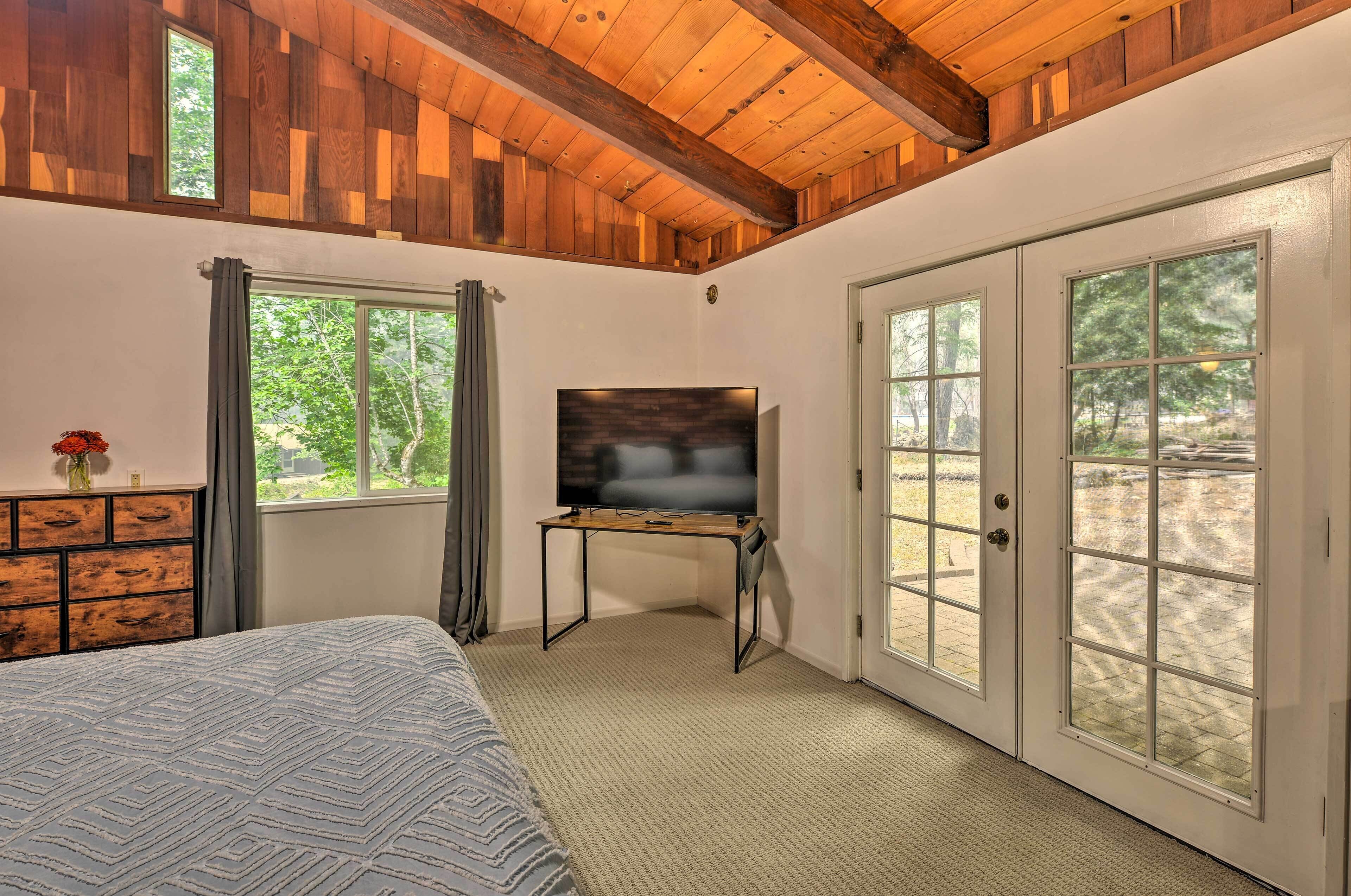 Un dormitorio con una cama, un televisor sobre un mueble bajo, un aparador y ventanas amplias.