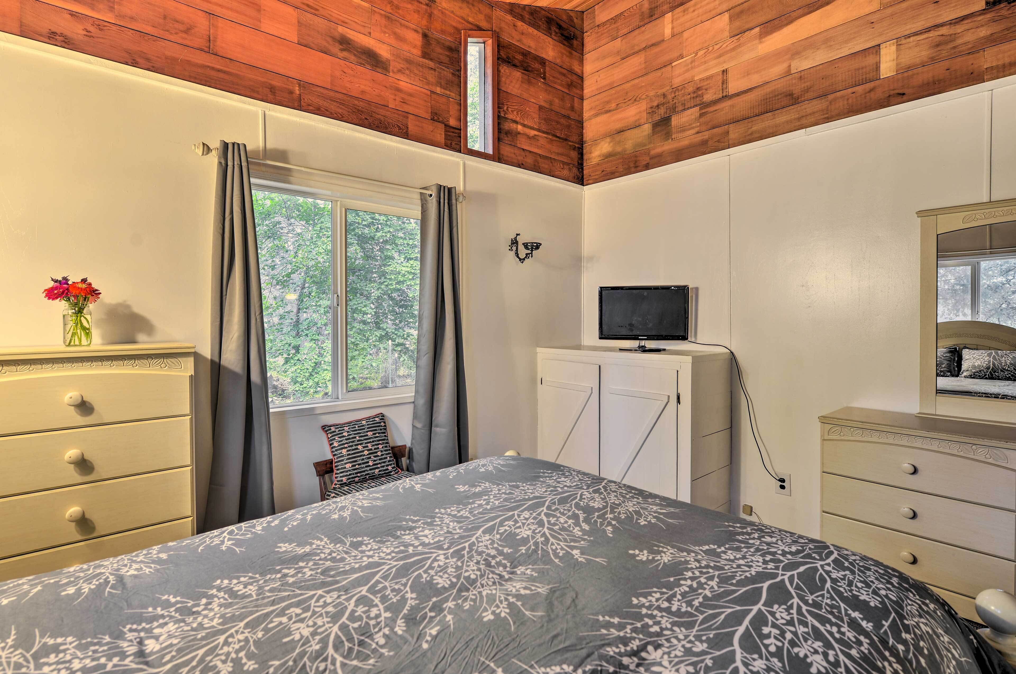 A bedroom with a bed, dresser, TV, and a window with curtains.