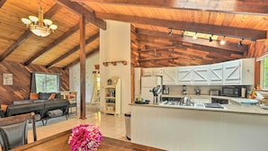 A spacious kitchen with white cabinets and a central island, a dining area with a wooden table and chairs, and a living room with a dark sofa and a chandelier. - Step-free Hawkins Bar Home Near Trinity River (Salyer)