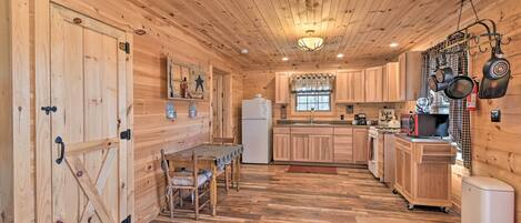 L’intérieur d’une cabane en bois comprend une table à manger, des chaises, un coin cuisine et un réfrigérateur.