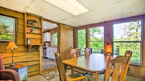 A dining area with a wooden table and chairs, a kitchen in the background, and large windows with a view of greenery. - Secluded 'mountain Home' 12 Mi to Tsali Area (Robbinsville)