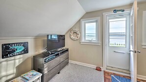 A room with a television, a dresser, a sign reading "SURFER LOUNGE", a window, and a door. - Sunset & Water Views in WWC on Sunset Lake (Wildwood Crest)
