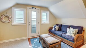 A cozy room with a sloped ceiling, a wicker sofa with cushions, a small ottoman, and a patterned rug. - Sunset & Water Views in WWC on Sunset Lake (Wildwood Crest)