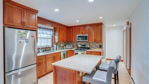 A modern kitchen with wooden cabinets, stainless steel appliances, and a central island with bar stools. - Woodstock Getaway w/ Hot Tub ~ 2 Mi to Dtwn! (Woodstock)