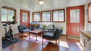 A room with a red door, wooden floors, a sofa, a chair, a table, and a bike. - Woodstock Getaway w/ Hot Tub ~ 2 Mi to Dtwn! (Woodstock)