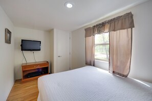 A bedroom with a bed, a television on a wooden stand, a window with curtains, and a door. - Winery Cabin in Fredericksburg w/ Wraparound Deck! (Fredericksburg)