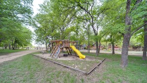A playground with a slide and climbing structures surrounded by trees. - Winery Cabin in Fredericksburg w/ Wraparound Deck! (Fredericksburg)