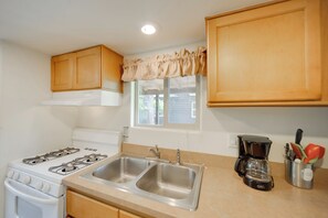 A kitchen with a stove, double sink, wooden cabinets, a window with a valance, and a coffee maker. - Winery Cabin in Fredericksburg w/ Wraparound Deck! (Fredericksburg)