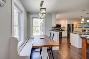 A modern kitchen with a wooden dining table, white cabinetry, and a large window providing natural light. - Stunning Wells Home w/ Fire Pit & Porch! (Wells)