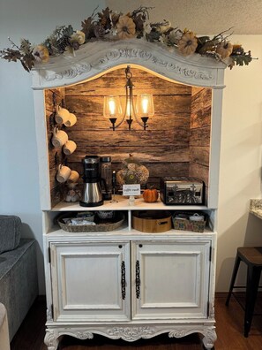 A white cabinet with a rustic wooden backdrop, a coffee maker, a toaster, and a decorative sign. - Penthouse at Notch (First Responder Owner) (Reeds Spring)