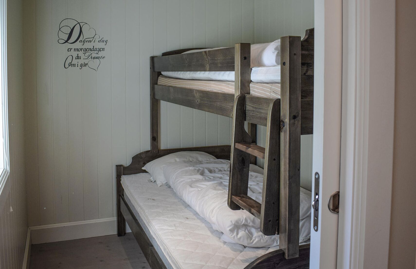 Una cama litera con ropa de cama blanca en una habitación con paredes de colores claros.