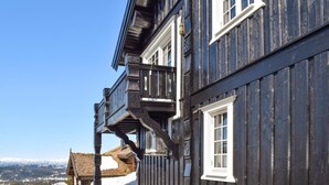 Ein traditionelles Holzhaus mit Balkon, großen Fenstern und Blick auf schneebedeckte Berge.