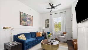A living room with a blue sofa, a round coffee table, a white armchair, and a ceiling fan.