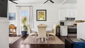 A modern kitchen with white cabinets, a microwave, and a stove. There is a dining area with a table and chairs, and a large potted plant.