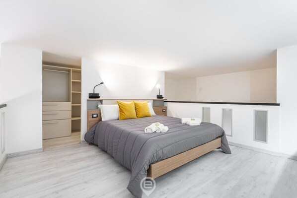 A modern bedroom with a grey bed, wooden headboard, and a walk-in closet. - Castello Loft Heaven (Cagliari)