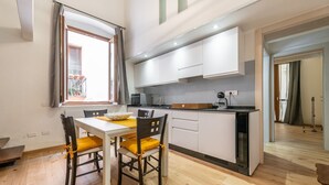 A modern kitchen with white cabinets, a dining table with two chairs, and a built-in oven. - Castello Loft Heaven (Cagliari)