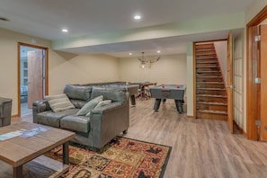 A spacious living room with a leather sofa, a coffee table, and a pool table. A staircase is visible in the background.