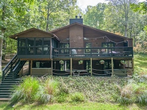 A two-story wooden cabin with a balcony, surrounded by lush greenery.