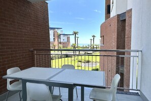 A balcony with a table and chairs, offering a view of a brick building and palm trees. - Frontemar Residenze sul mare D6 - Carrraro Immobiliare Jesolo (Lido di Jesolo)