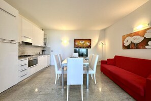 Une cuisine moderne avec des meubles blancs, une table à manger avec des chaises, un canapé rouge et des œuvres d’art accrochées aux murs.