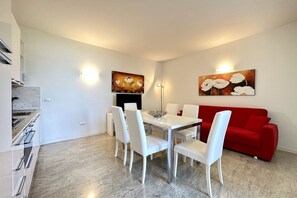 A modern living room with a dining area, white furniture, and two wall-mounted light fixtures.