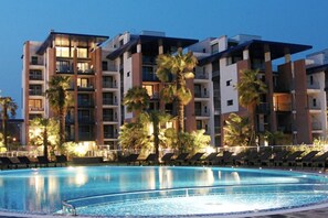 Ein modernes Hotel mit Schwimmbad, Palmen und Liegestühlen.