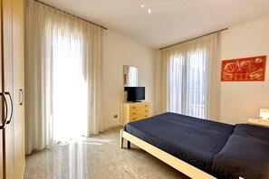 Ein Schlafzimmer mit einem Bett, einem Fernseher auf einem Schrank, einem Schminktisch und einem Gemälde an der Wand.