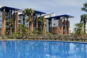 A modern hotel with a pool, palm trees, and lounge chairs. - Frontemar Residenze sul mare D6 - Carrraro Immobiliare Jesolo (Lido di Jesolo)