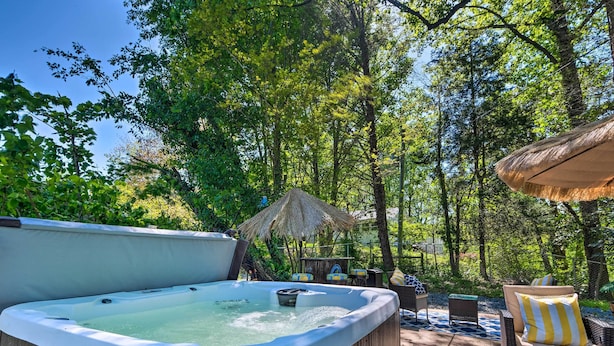 Un bain à remous entouré de meubles en osier et abrité par un parasol en chaume, le tout situé dans un écrin de verdure, au cœur d’une zone boisée.