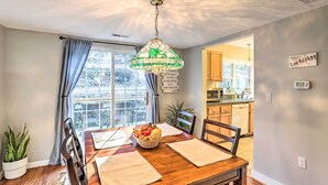 A dining area with a wooden table, chairs, a chandelier, a window with curtains, and a view of the kitchen. - 'carefree Cottage' < 6 Mi to Downtown Asheville! (Asheville)