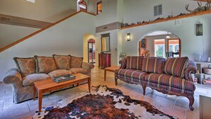 A spacious living room with a high ceiling, a large window, and a rustic decor including a cowhide rug and wooden furniture.
