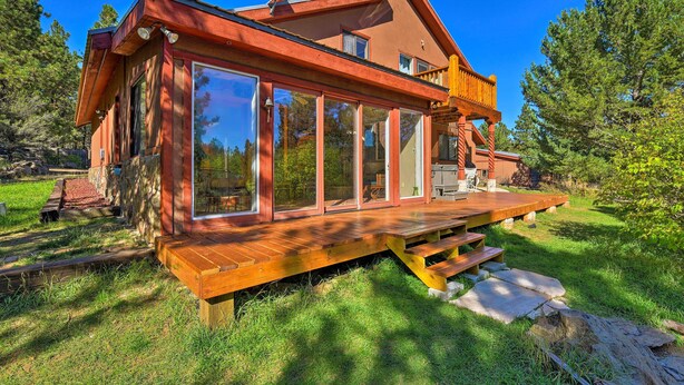 A modern wooden house with large glass windows, a deck, and a stone pathway.