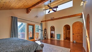 A spacious bedroom with a large bed, wooden floors, a ceiling fan, and a view of a balcony.
