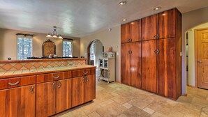 A spacious kitchen with wooden cabinets, a large island, and a view of trees through the windows.