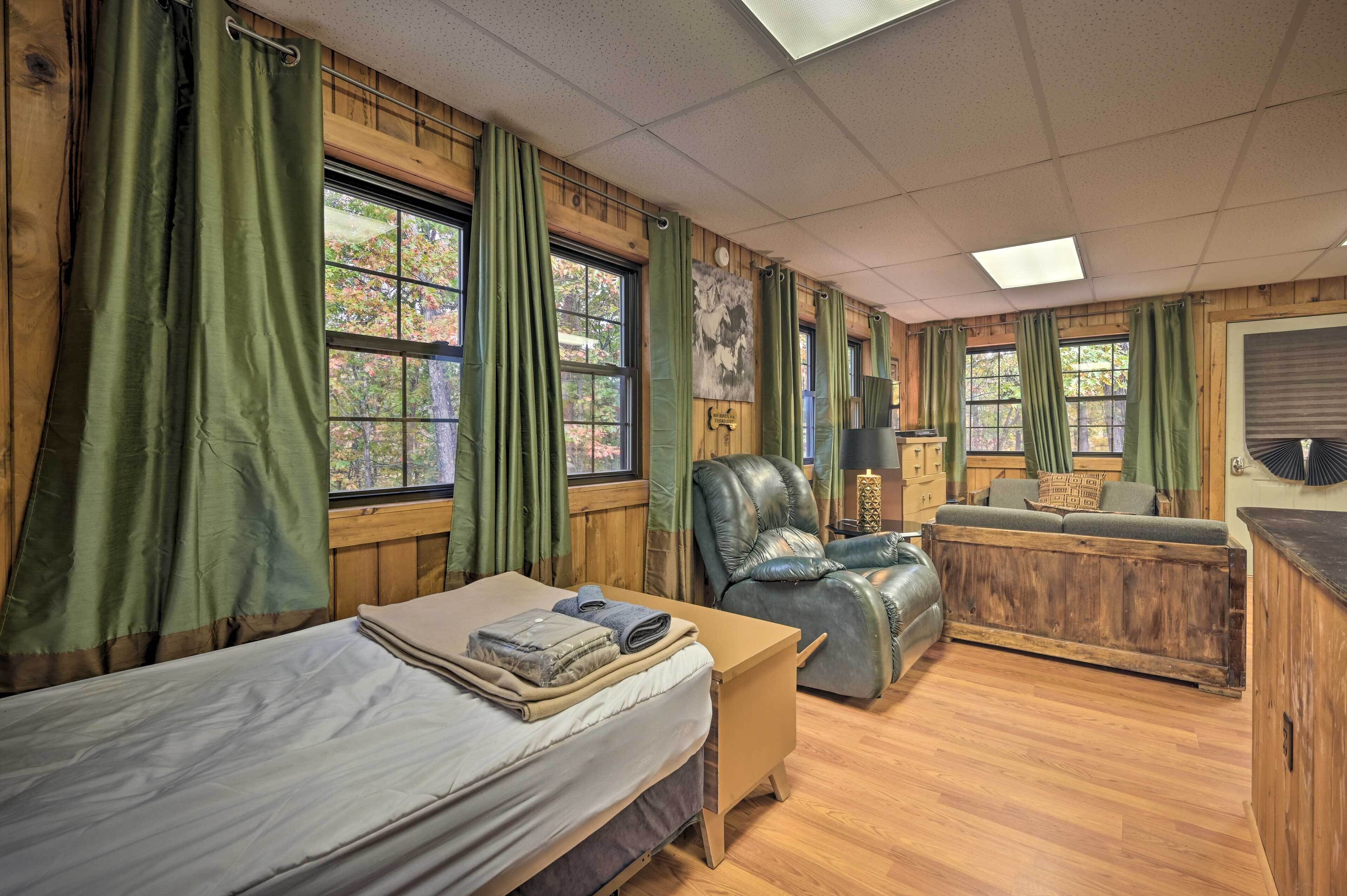 A room with a bed, a sofa, and a desk. There are curtains on the windows, and a painting on the wall.