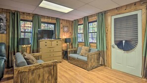 A cozy room with wooden walls, a sofa, a chair, a TV, and a door with a fan. - Cheyenne Ranch Retreat Near Raystown Lake! (Huntingdon)