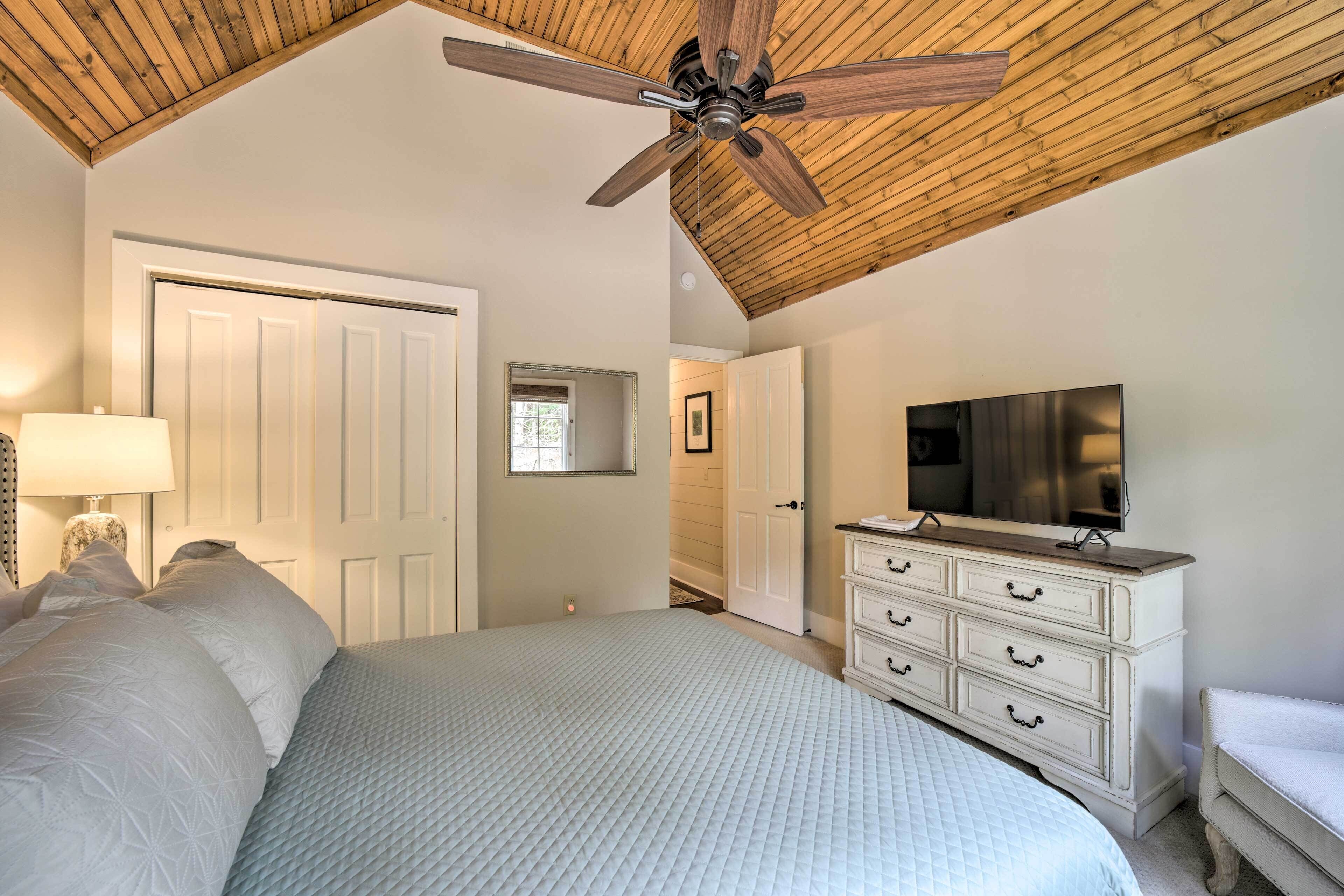 A bedroom with a bed, a dresser, a TV, a ceiling fan, and a door.