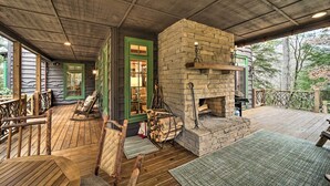 A wooden deck with a stone fireplace, rocking chairs, and a covered porch area. - Beautiful Trillium Home Next to Waterfall! (Cashiers)