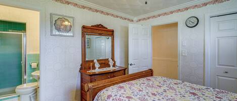 A bedroom with a bed, a dresser, a mirror, a door, and a bathroom with a toilet and shower.