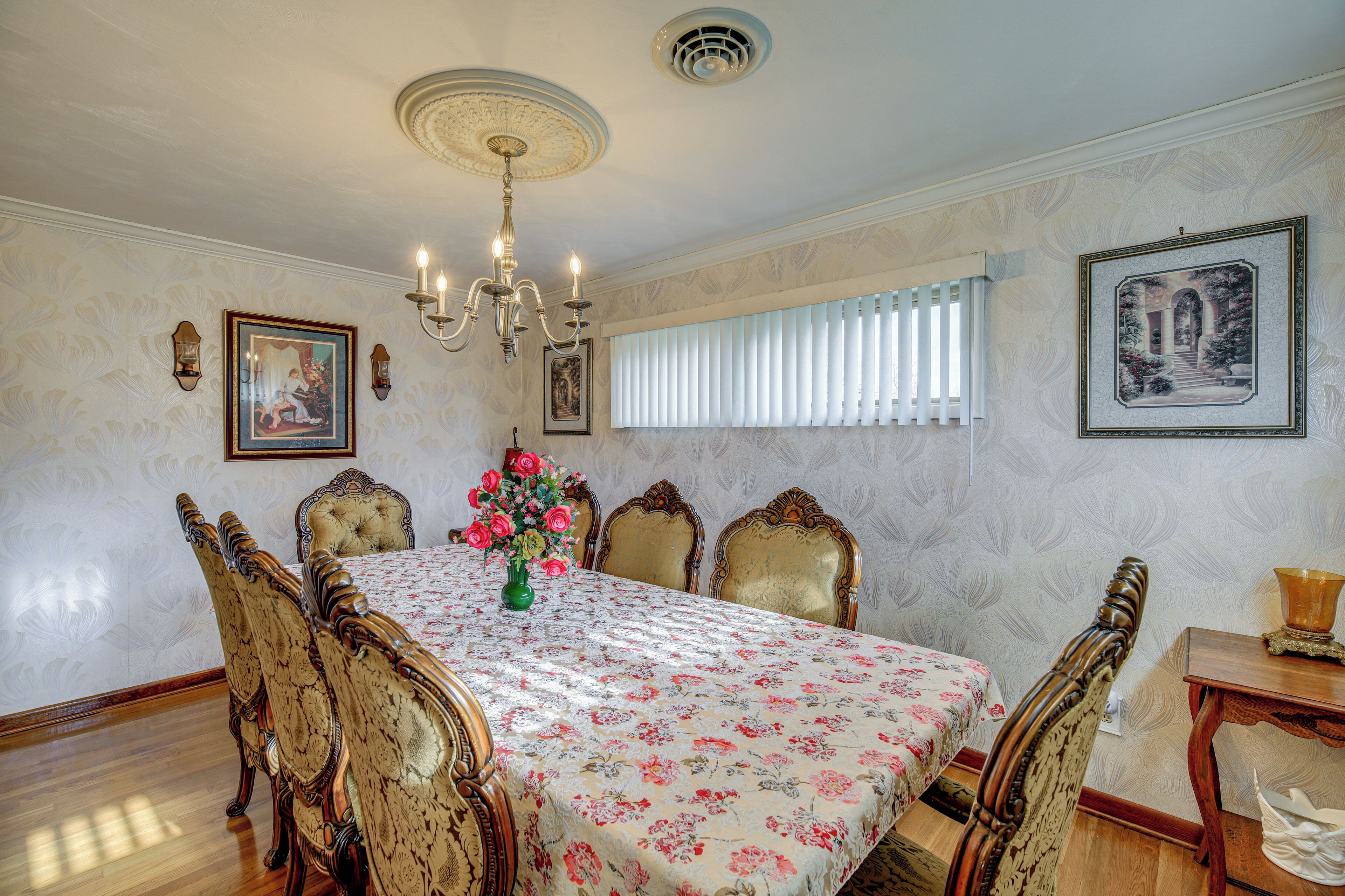 A dining room with a floral tablecloth, ornate chairs, a chandelier, and framed artwork on the walls.