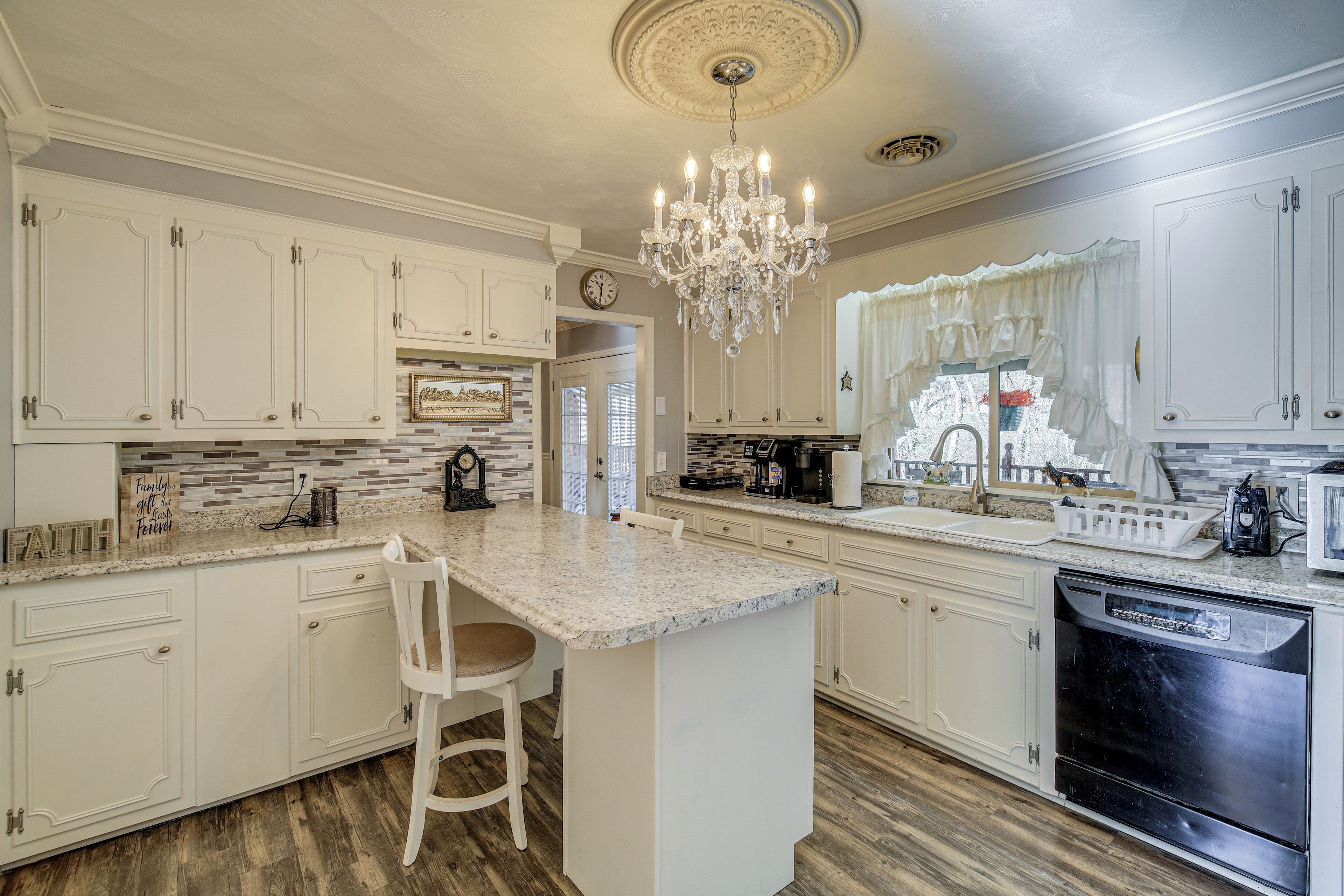 A spacious kitchen with white cabinetry, a central island, a chandelier, and a dishwasher.