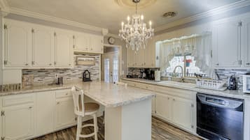 A spacious kitchen with white cabinetry, a central island, a chandelier, and a dishwasher.