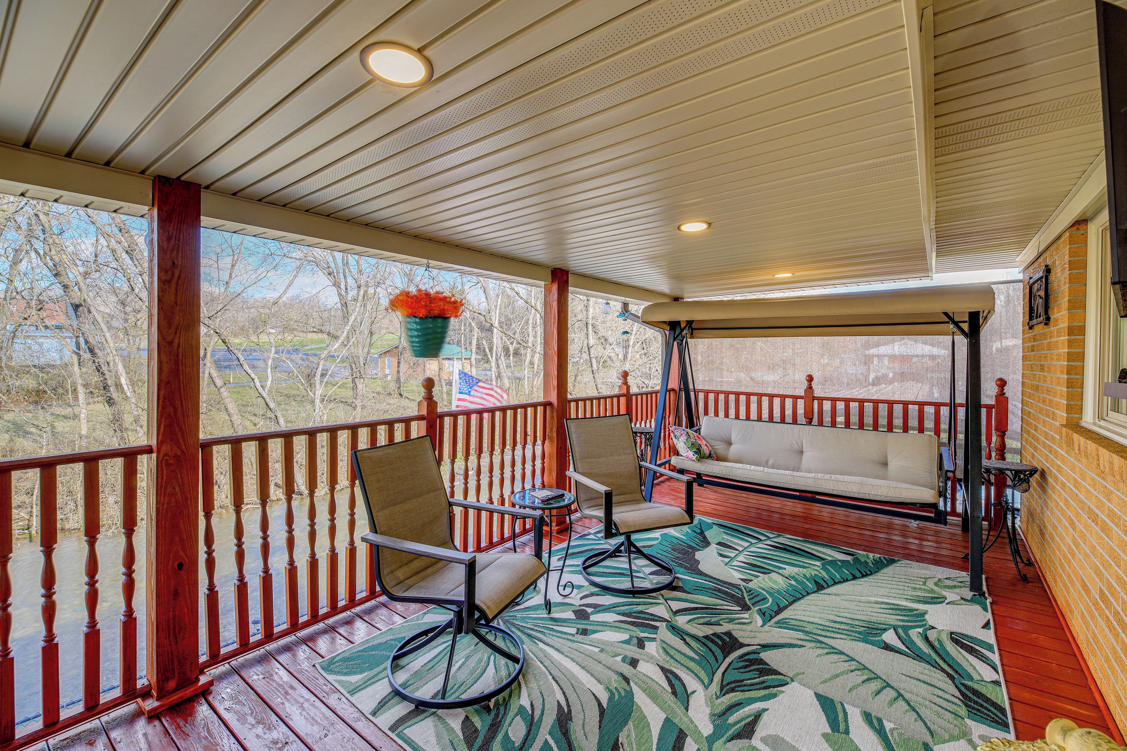 A covered porch with a wooden railing, a bench, and two chairs.