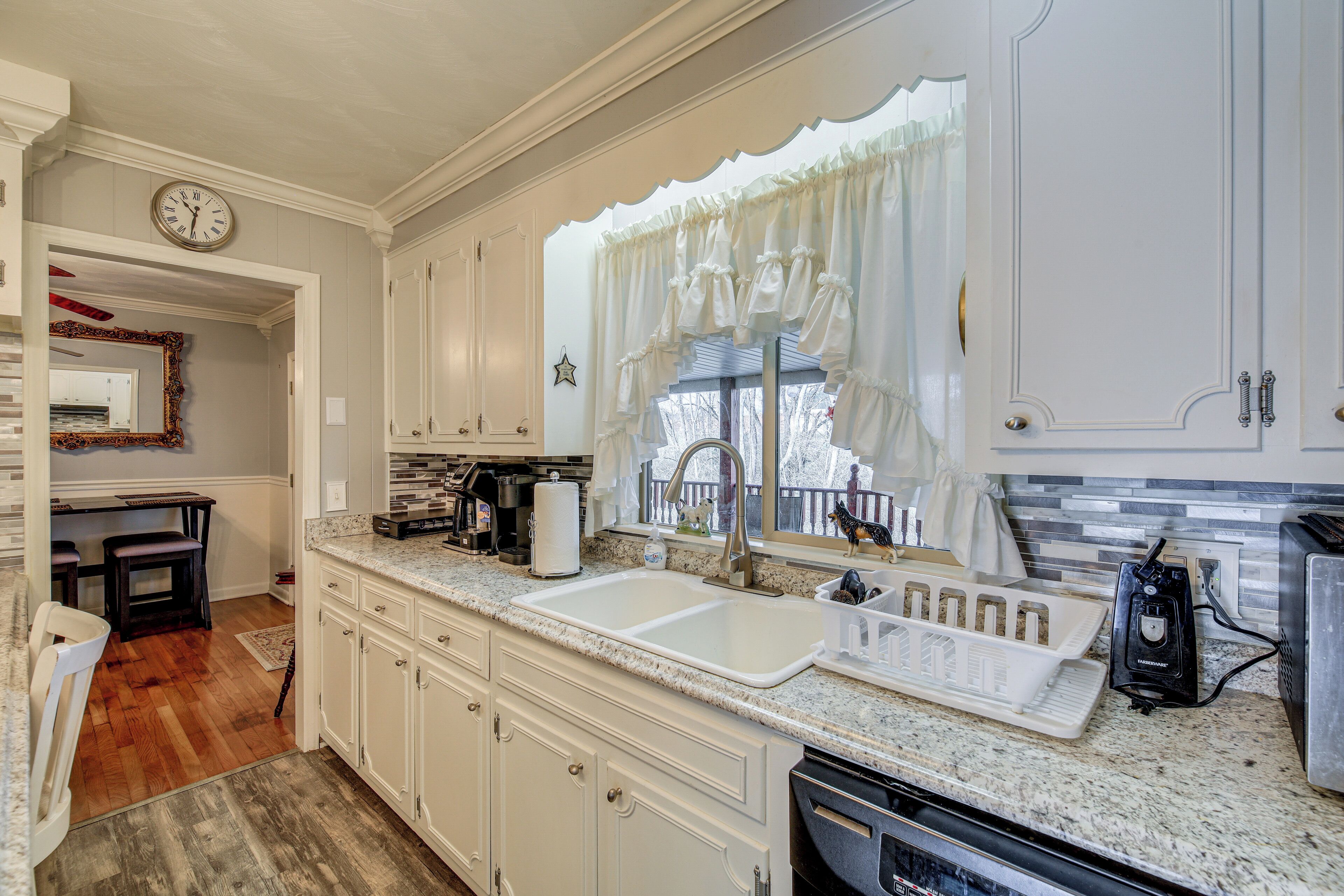 A kitchen with white cabinets, a double sink, and a window with white curtains.
